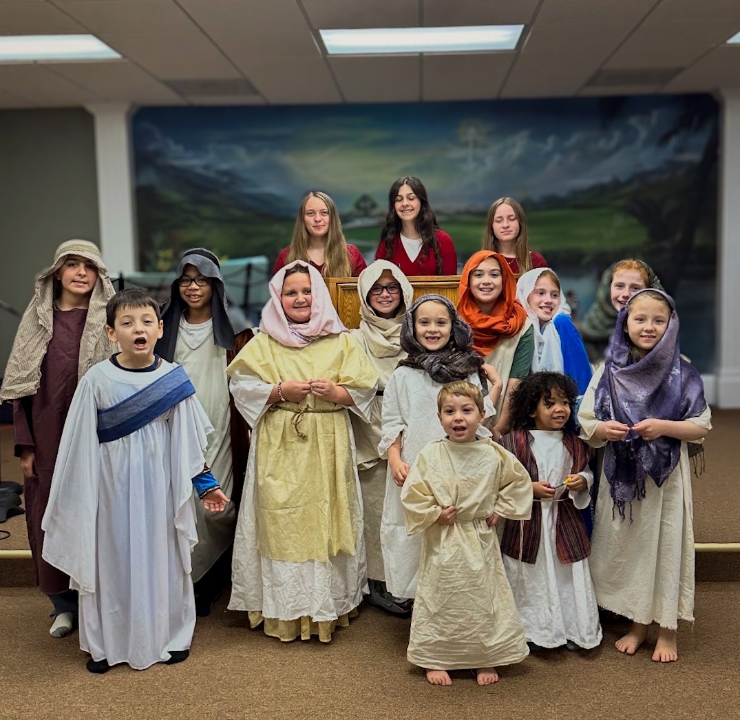 Children and adults dressed in biblical costumes pose together, smiling in a church setting, likely for a performance or community event.