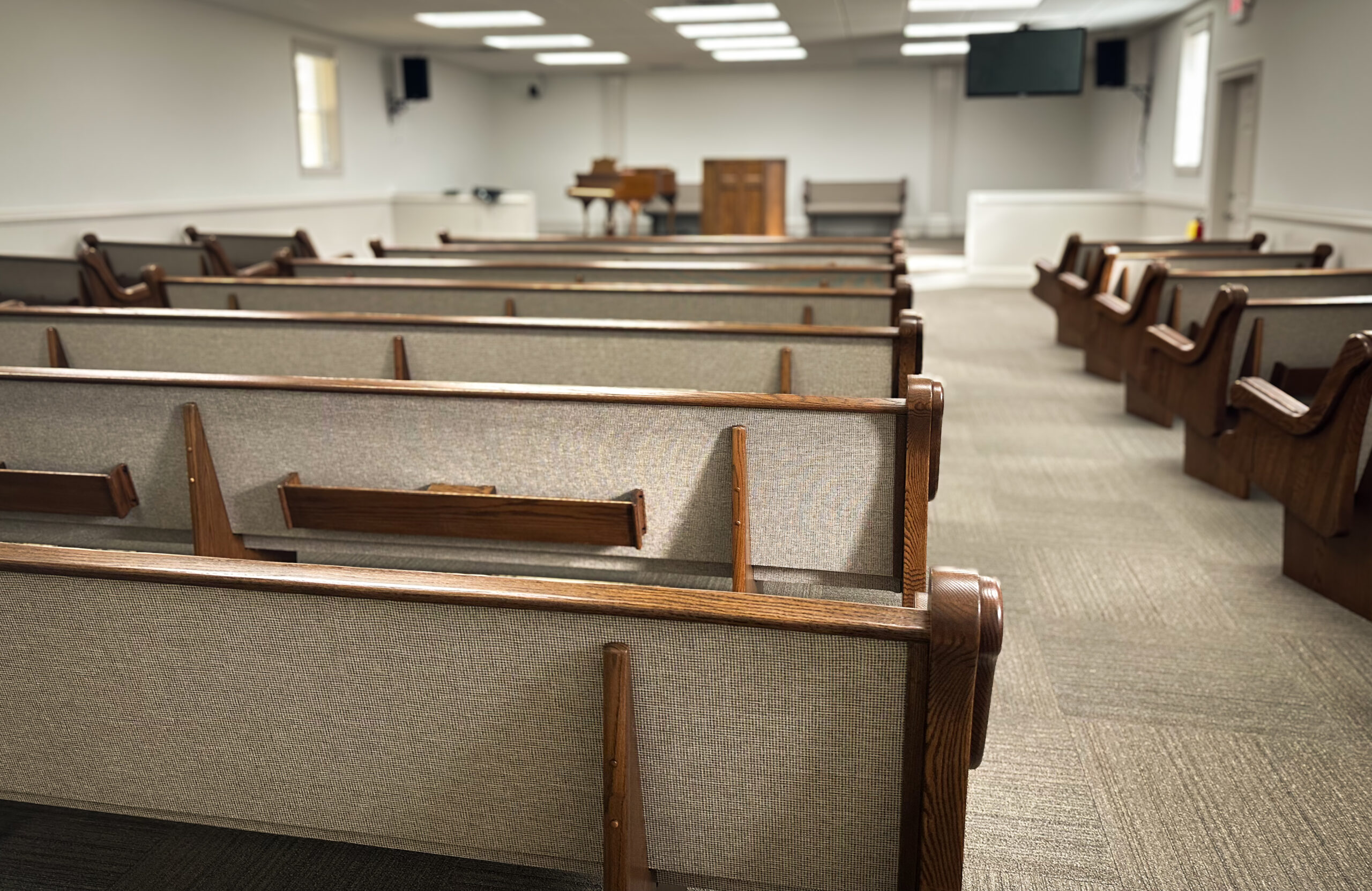 Empty church pews lead to a simple altar and a piano, creating a serene atmosphere for worship or reflection.